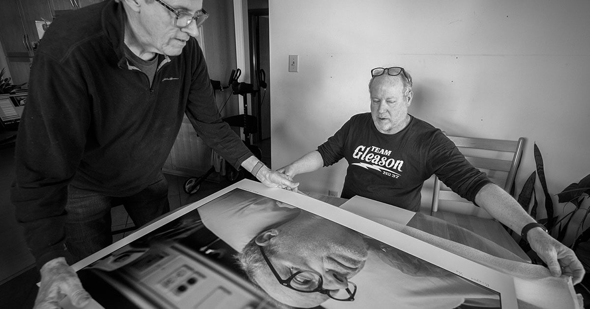 Two people positioning a large framed black-and-white photograph on a table, preparing it for display or signing.