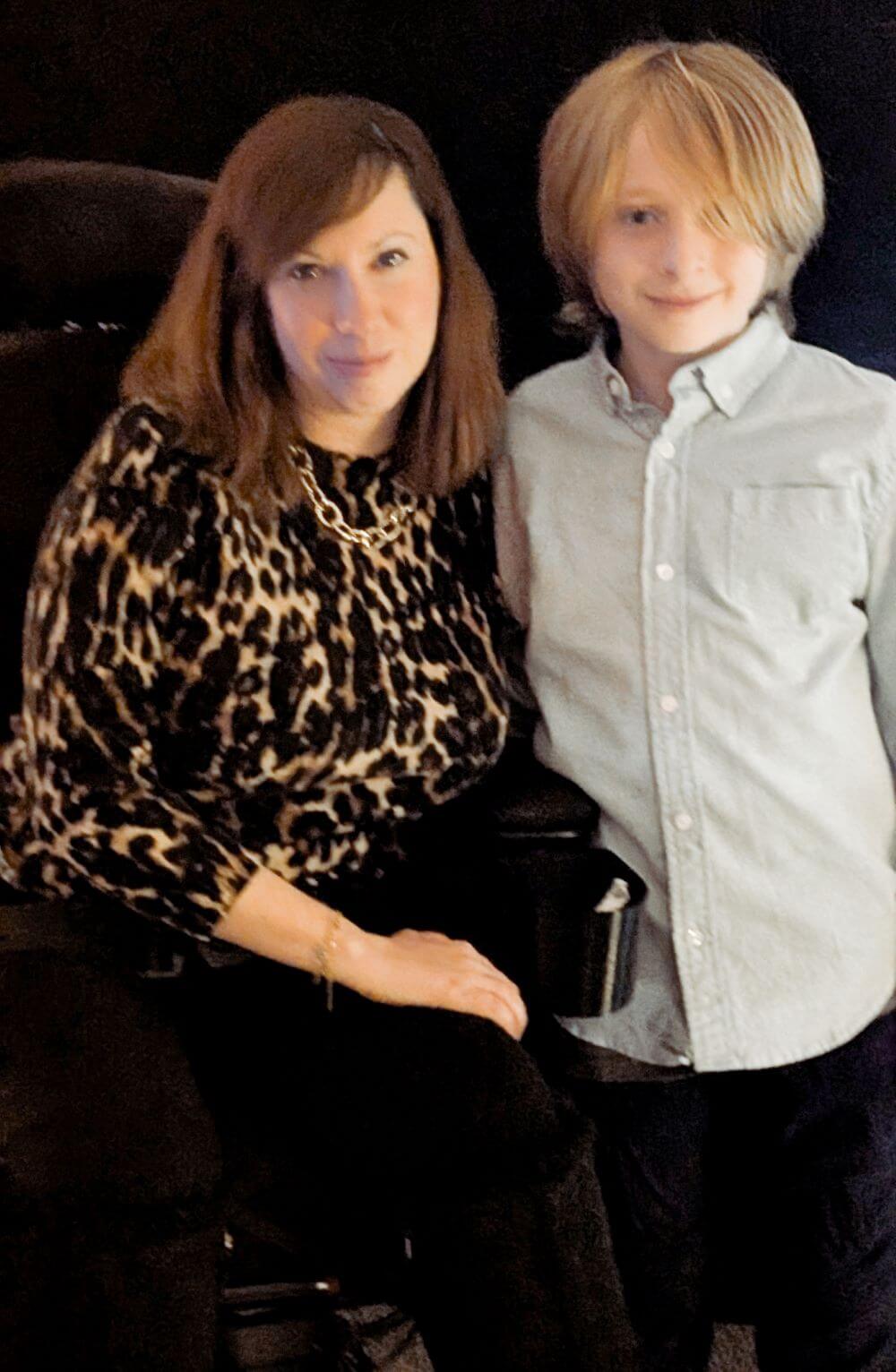 An adult seated next to a child, both facing the camera, in an indoor setting.