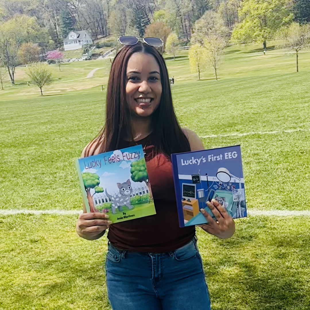 Joseannie Martinez smiling with her children’s books, Lucky Feels Fuzzy, and Lucky’s First EEG. 