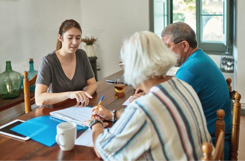 three people, 2 women and a man, sitting at a table looking over documents and talking
