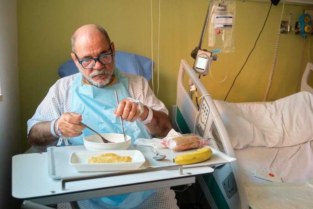 Hospitalized mature man eating a healthy meal in his hospital bed