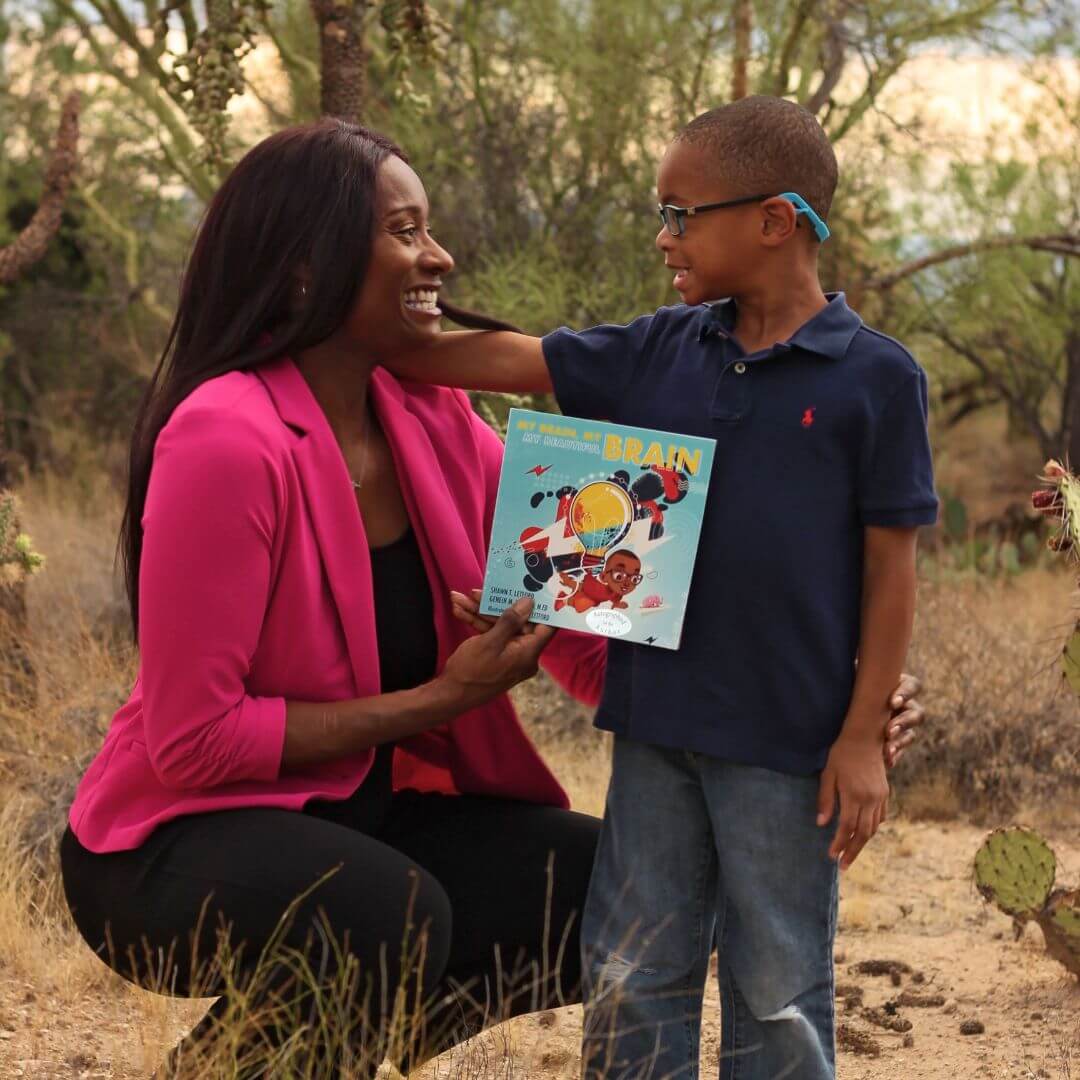 An adult and a child outdoors holding a copy of the children's book My Brain, My Brain, My Beautiful Brain.