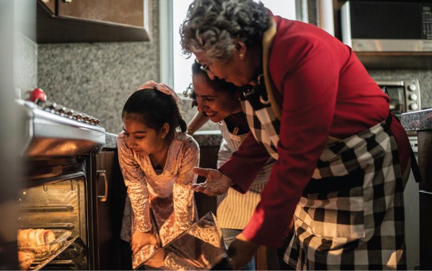 3 generations of women looking into an open oven with something baking inside