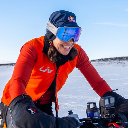Rebecca Rusch outside in the winter smiling wearing an orange jacket and snow goggles