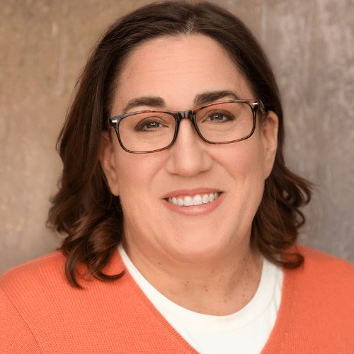 Beth Pinsker smiling while wearing glasses and an orange sweater.