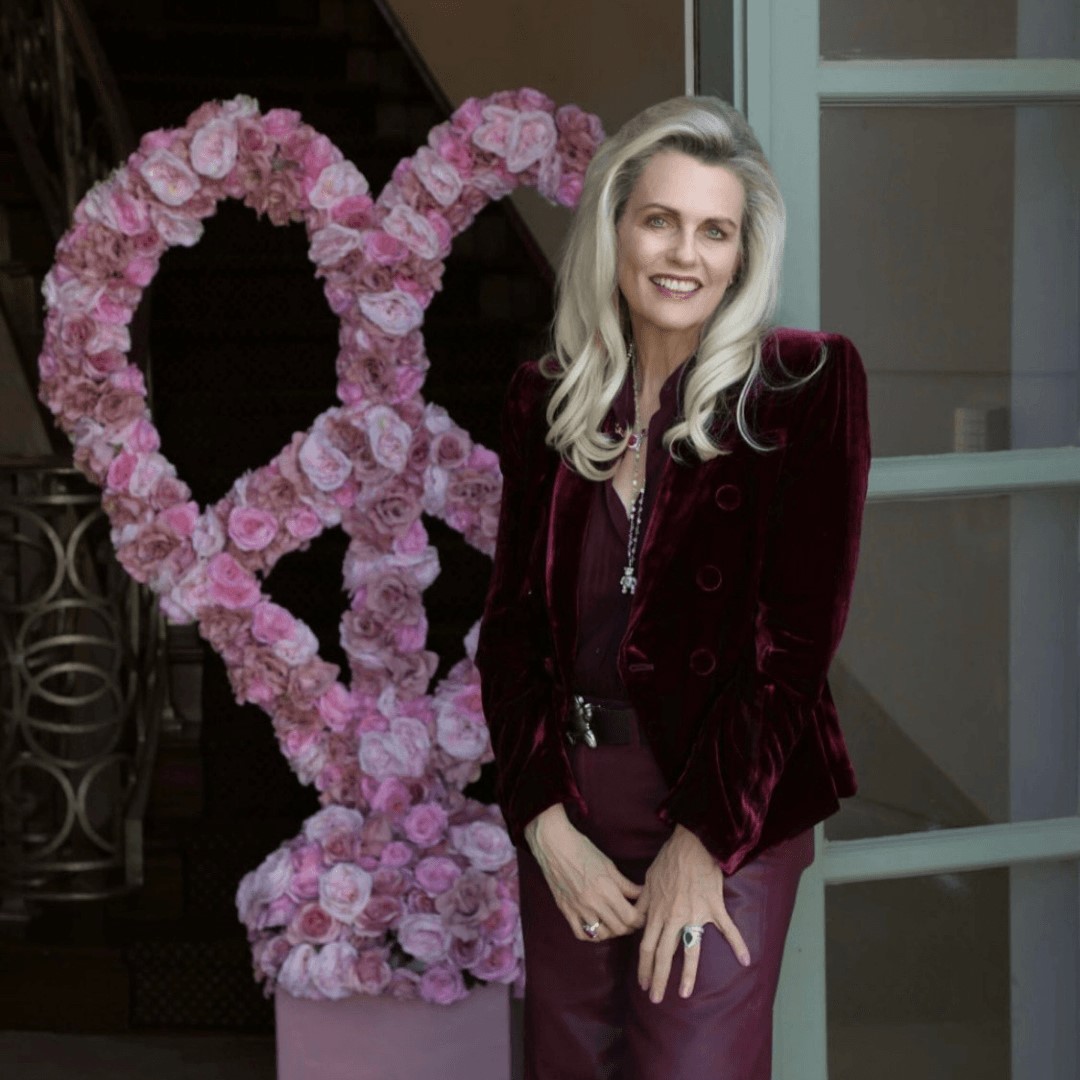 Woman in a burgundy outfit smiling beside a large pink floral peace sign display indoors.
